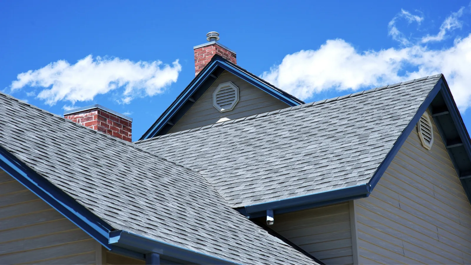 Gray shingle rooflines with brick chimneys against a bright blue sky