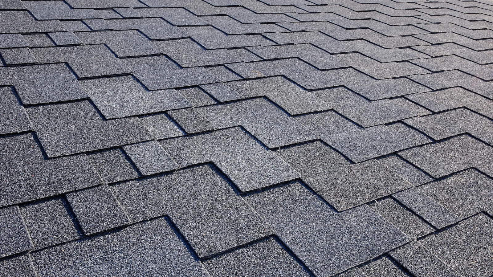 Staggered pattern of dark gray asphalt shingles viewed closely
