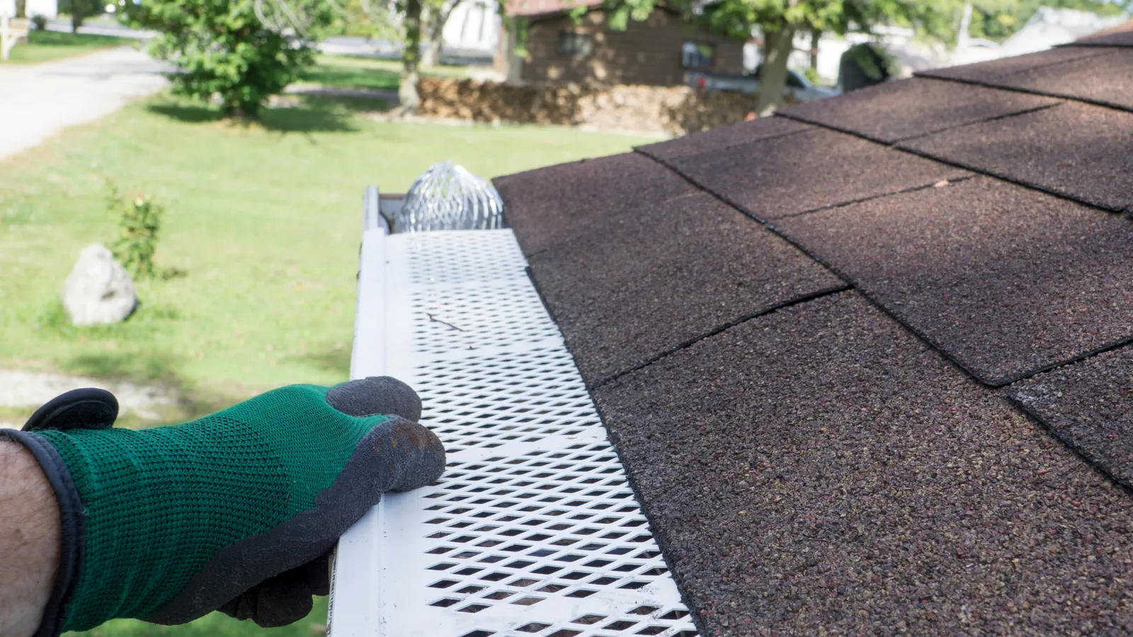 A roofer's gloved hand securing perforated gutter guard