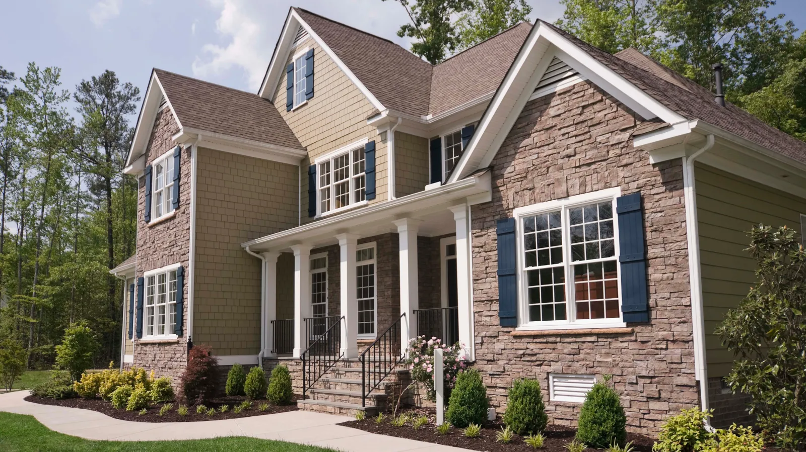 Stacked stone and shake siding on a two-story home beneath a brown shingle roof