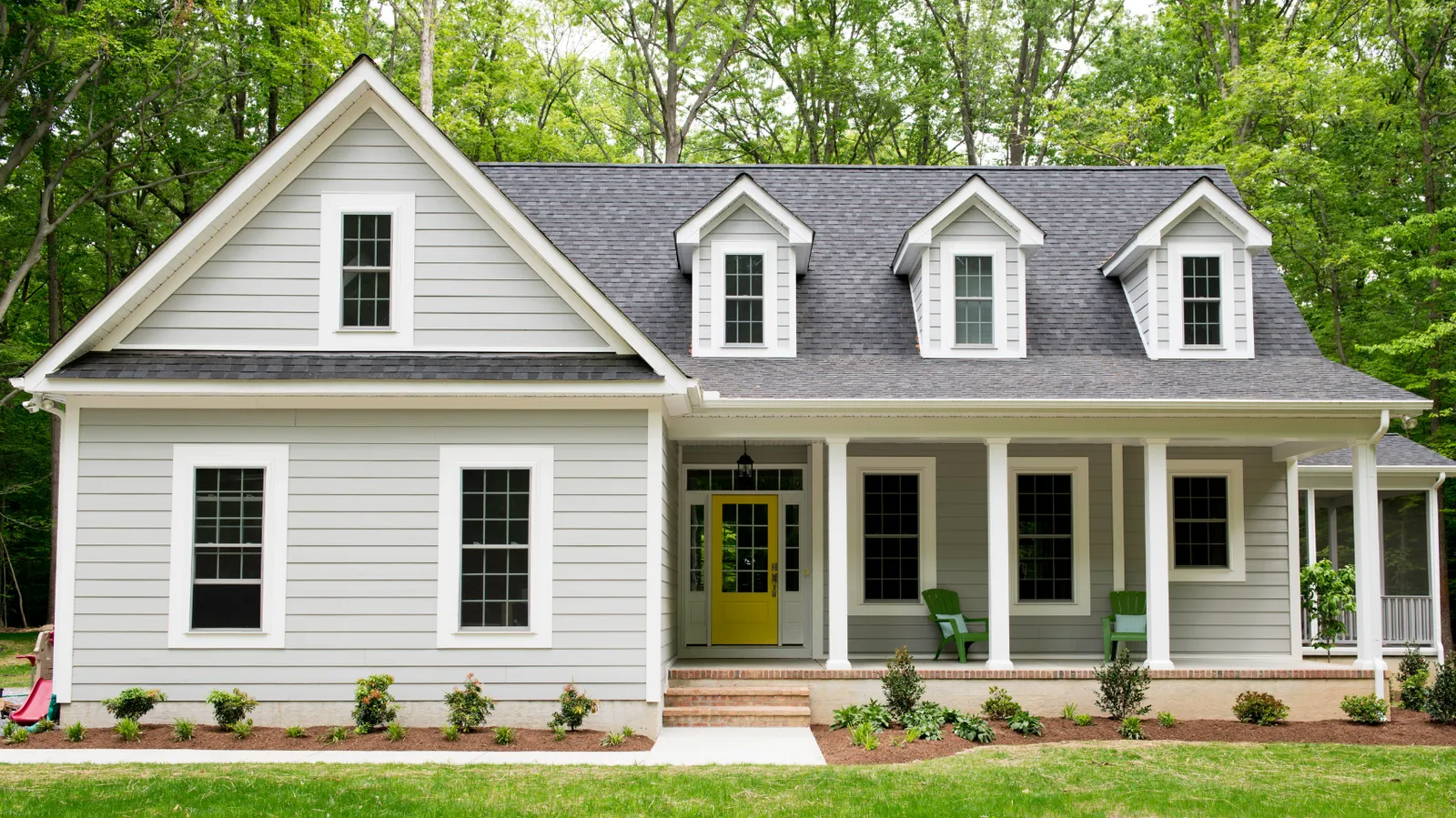Gray house with a yellow front door and dark gray shingle roof with dormers