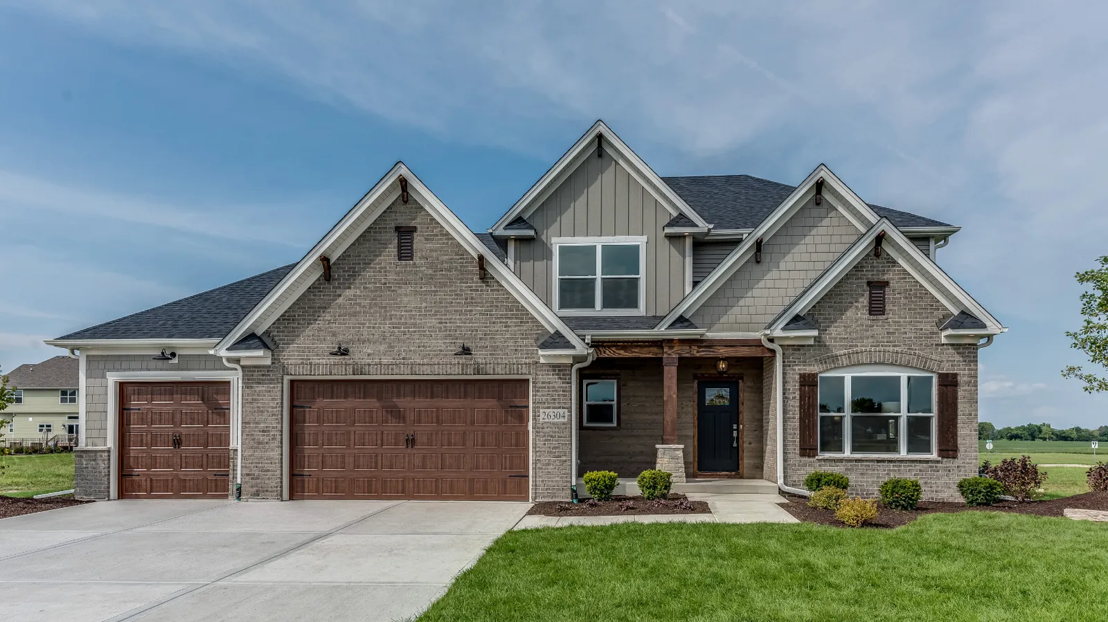 Dark shingle roof on a gray brick craftsman home with wood garage doors