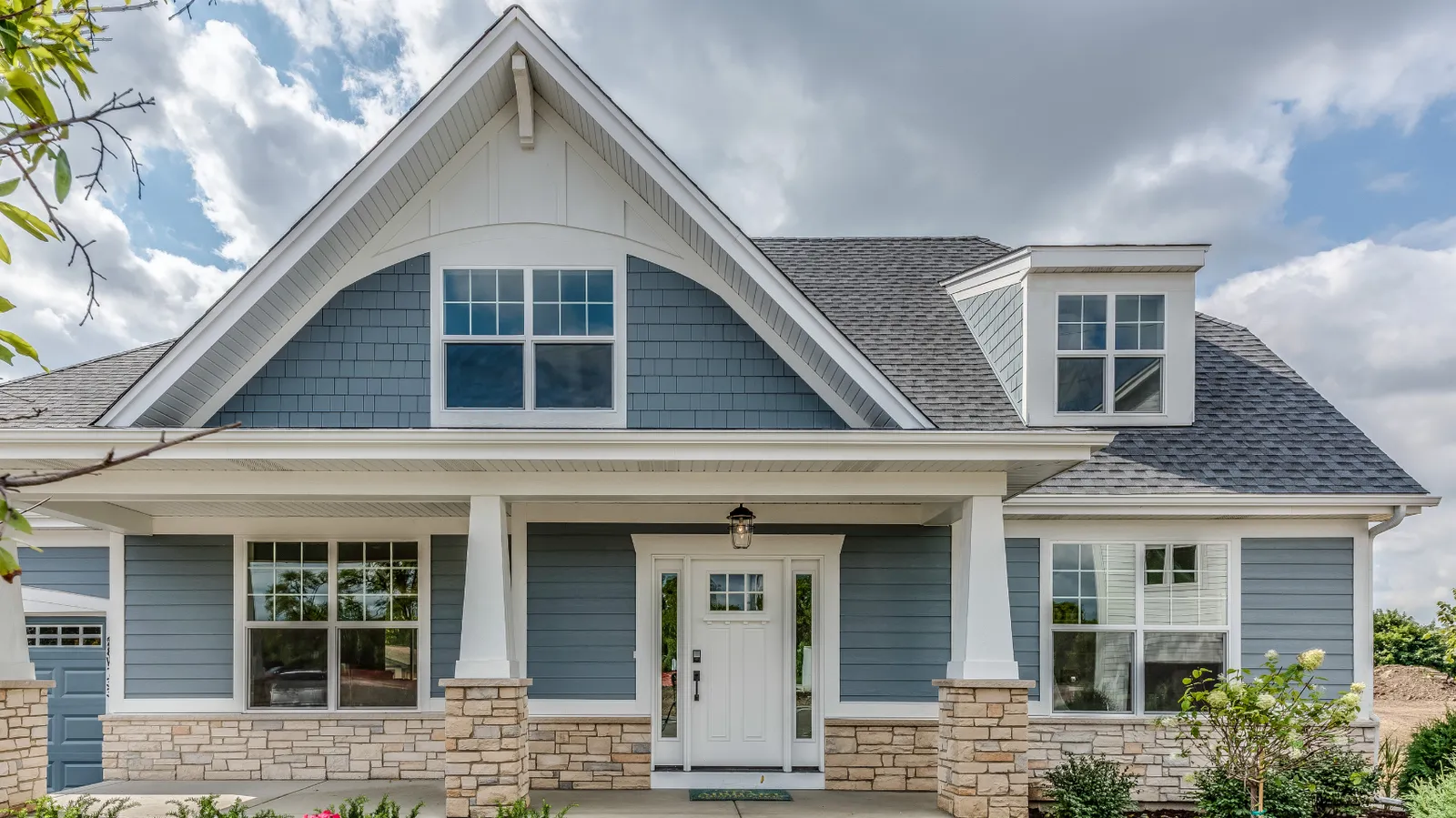 Blue craftsman home with gray shingle roof and stone porch columns