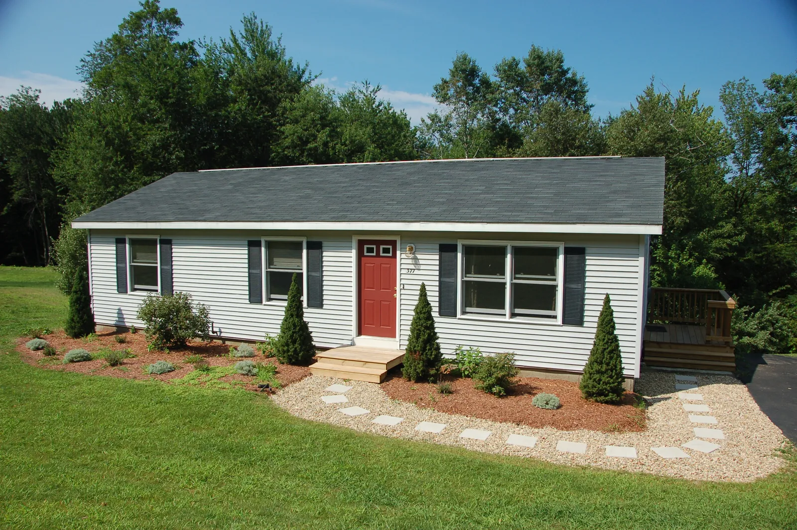 Small ranch home with dark shingle roof and red front door